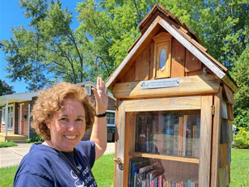 Ms. Kuenzel is standing in front of her Little Free Library.